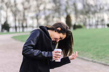 a beautiful girl in a black coat , walks in the Park and drinking coffee