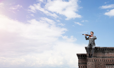Handsome violinist in glasses on building edge play his melody