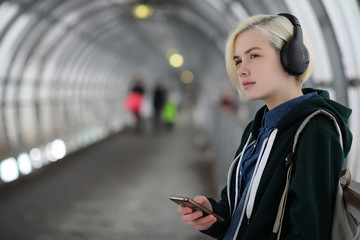 Young girl listens to music in big headphones in the subway