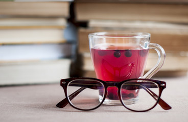 Blueberry tea in a glass cap with   eyeglasses  behind the books  background.