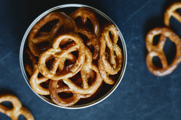 Crunchy pretzels appetizer in a metal jar against black background. Top view.