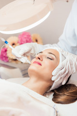 Fototapeta na wymiar Beautiful woman relaxing during non-invasive facial treatment for rejuvenation in a contemporary beauty center with innovative equipment
