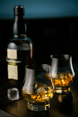 Whiskey in glasses with ice on rustic background