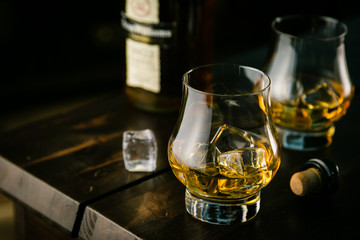 Whiskey in glasses with ice on rustic background