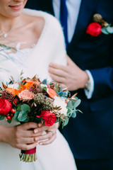 Newlyweds with a rustic wedding bouquet. Groom embrace woman by the waist. Soft focus on the flowers.