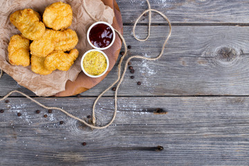 Wooden board with tasty chicken nuggets and sauces on table