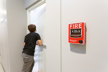The man running open emergency exit door is and fire alarm on the wall next to the door.