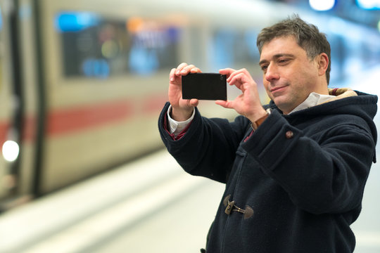 Passenger taking photos with his smartphone from railway station platform