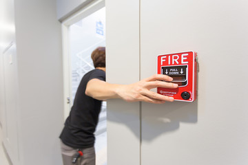 The man running and hand is pulling fire alarm on the wall next to the emergency exit door.