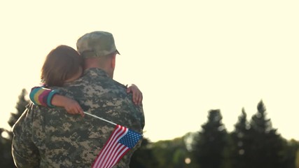Soldier in camoubackgrounde hugging daughter outdoors, back view. Girl see off father huging him before military mission.