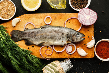 Fresh fish with herbs and spices on vintage cutting board on dark background, top view