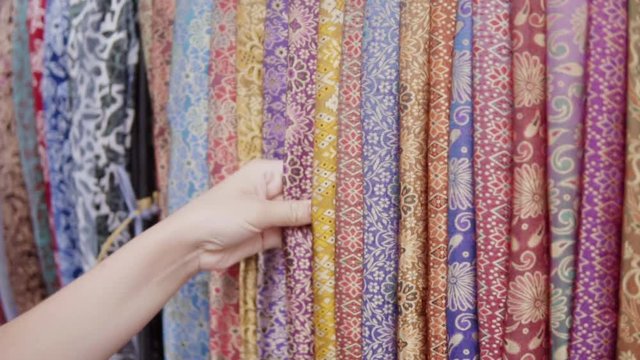 Stand of the colorful embroidered with threads and stamp print clothes in different colours at the traditional etnic asian market. Womans hand trying the quality of the textile material