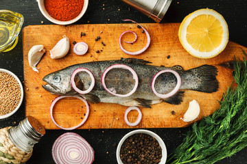 Fresh fish with herbs and spices on vintage cutting board on dark background, top view