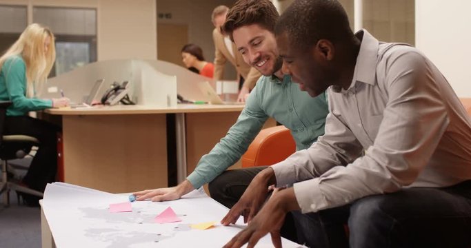 4K 2 Businessmen in a meeting, looking at world map & brainstorming with sticky notes. Slow motion.