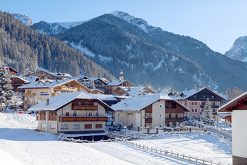 Snowy alpine village in Italy illuminated by sun with mountains in the background. Italian Dolomites, Trentino-Alto-Adige region, Italy