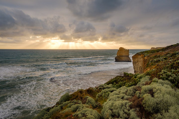 Single rock in the ocean with cliffs in the foreground at sunset