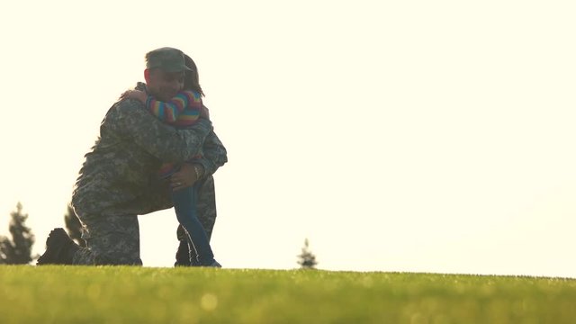 Miltary man return from the army meeting his daughter. Soldier standing on one knee with embracing arms in the air.