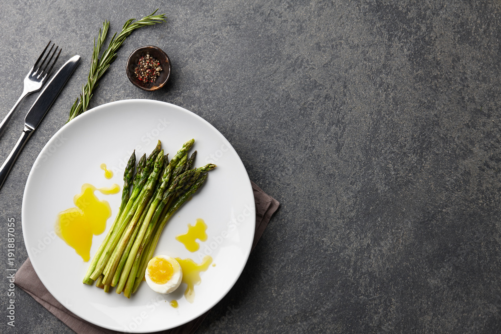 Wall mural Baked asparagus with boiled egg in big white plate on stone background, top view