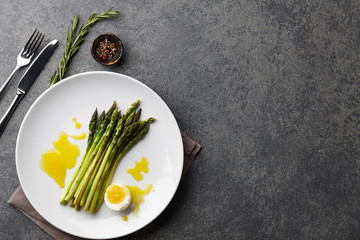 Baked asparagus with boiled egg in big white plate on stone background, top view