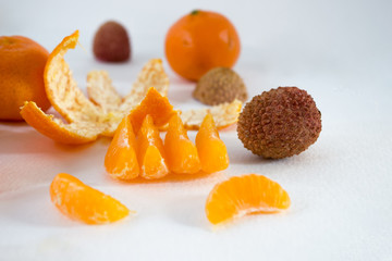 Mandarins on a white background with lobule, peel, citron and litchi. Side view, close. Citrus reticulata. Litchi chinensis.