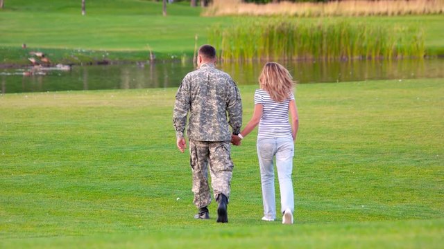Back view military man on date in a park lawn. Happy soldier with woman on glade, rear view.