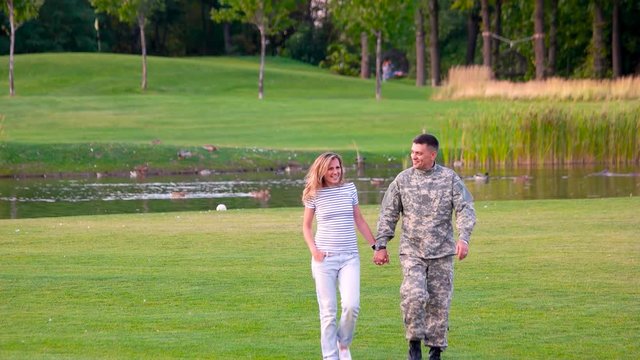 Romantic couple holding hands and walking, front view. Man in military uniform with woman in a park.