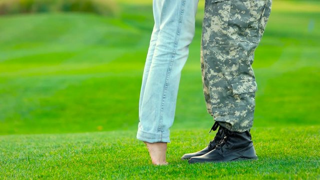 Woman stand on her toes to kiss her soldier boyfriend. Young military couple kissing each other, homecoming concept.