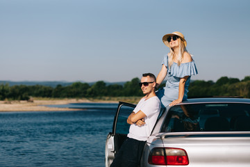 Happy traveler couple standing near car open trunk and watch the sunrise