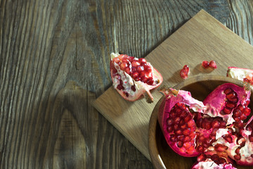 Pomegranate seeds in a wooden bowl, next to the pieces of pomegranate and a pomegranate.