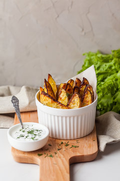 Delicious roasted potatoes garnished with parsley. Baked potato slices with sour cream sauce on white plate.