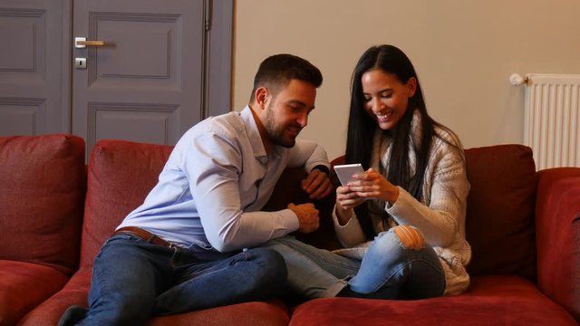A beautiful young couple in the living room discussing content on a smartphone.
