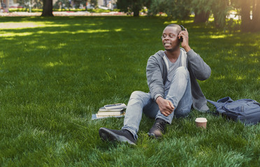 Smiling african-american student listening to music in park outdoors