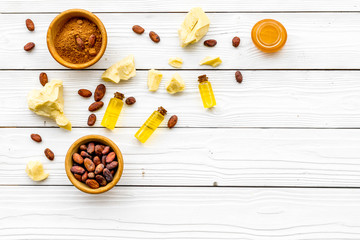 Pieces of cocoa butter and cacao powder in bowl for homemade cosmetics. White wooden background top view space for text