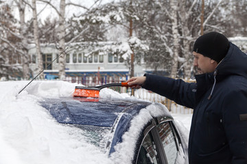 man brushes a car covered with snow