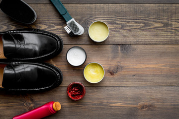 Fototapeta na wymiar Shoe polish, brushes, wax near black shiny leather shoes on dark wooden background top view copy space