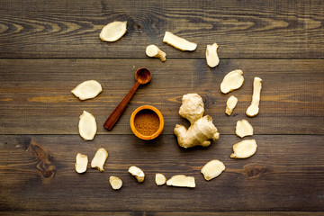 Spice and condiment. Ground ginger in small bowl near ginger root on dark wooden background top view