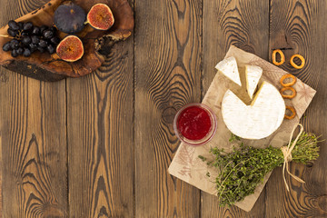 Cheese served with jam, figs, crackers and herbs on a wooden background.