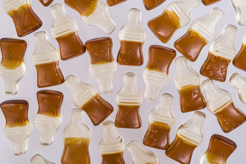Chewing marmalade bottles of cola on light background.