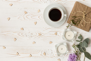 Top view of coffee, gifts, hearts, candles, flowers on white wooden table. Background with free space for text.