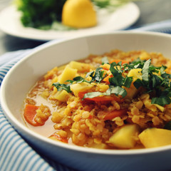 Red lentil stew on the round white plate. Vegetarian dish with potato, carrot and turmeric. European cuisine. Colorful vegan lunch. Selective focus.
