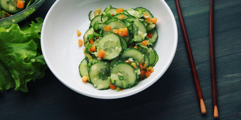 Chinese cucumber salad on the white plate. Top view. Chopsticks. Asian cuisine. Bell pepper, cucumber and sesame seeds. Wide photo. Vegetarian dish. Wide photo.