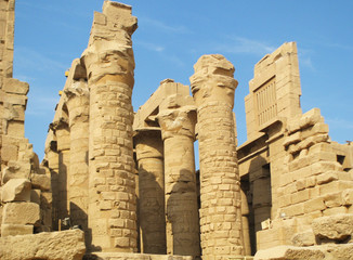 Large columns and ruins of stone walls in the ancient city of Luxor in Egypt. The sun beautifully illuminates buildings against the blue sky, forming bright and contrasting colors.