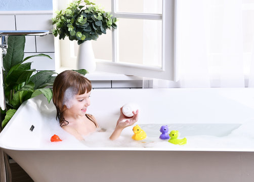 Happy little baby girl kid sitting in bath tub  in the bathroom