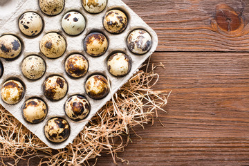 Quail eggs in a box and straw on a wooden table. Top view