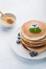 A stack of delicious pancakes with honey and blueberries on a light blue background