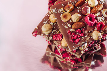Broken chocolate bars decorated with nuts and raspberry on pink background