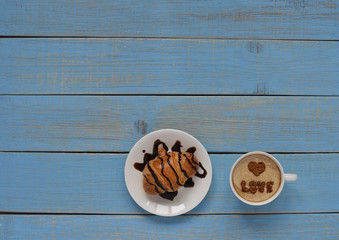 A croissant with liquid chocolate / a cup of coffee with cream and symbols of love on the foam:  a word 