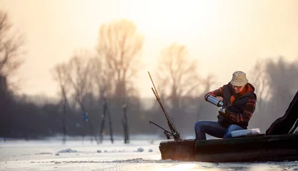 Fotobehang Fishing on ice- senior man sitting on frozen lake and drink tea © luckybusiness