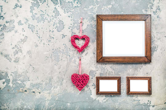 Photo or picture frames blanks and pair of handmade Valentine's day love hearts hanging on vintage aged grunge textured concrete wall background. Retro old style filtered photo