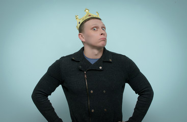 An arrogant and selfish man with a golden crown above his head scornfully looks forward isolated on blue background.